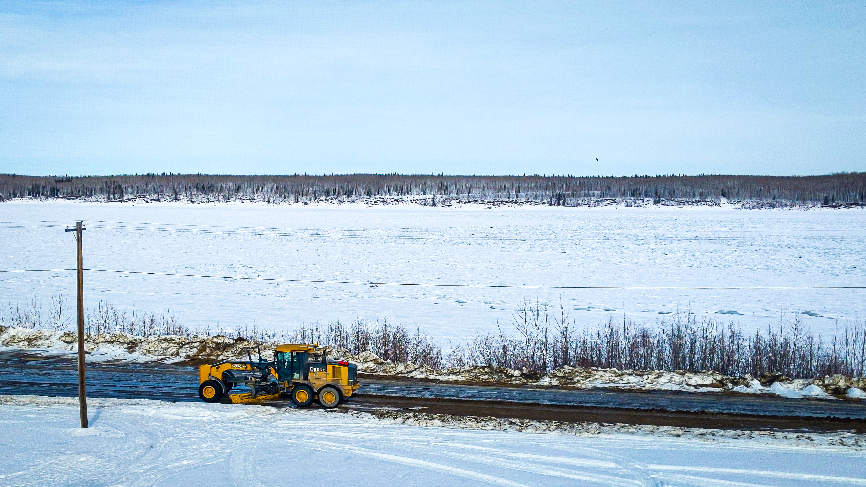 A grader passes along a Fort Simpson riverside road in March 2019