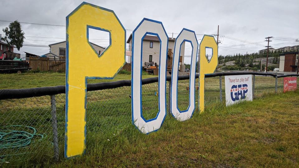 A large sign reading 'Poop' sits at a Yellowknife ballpark in July 2019
