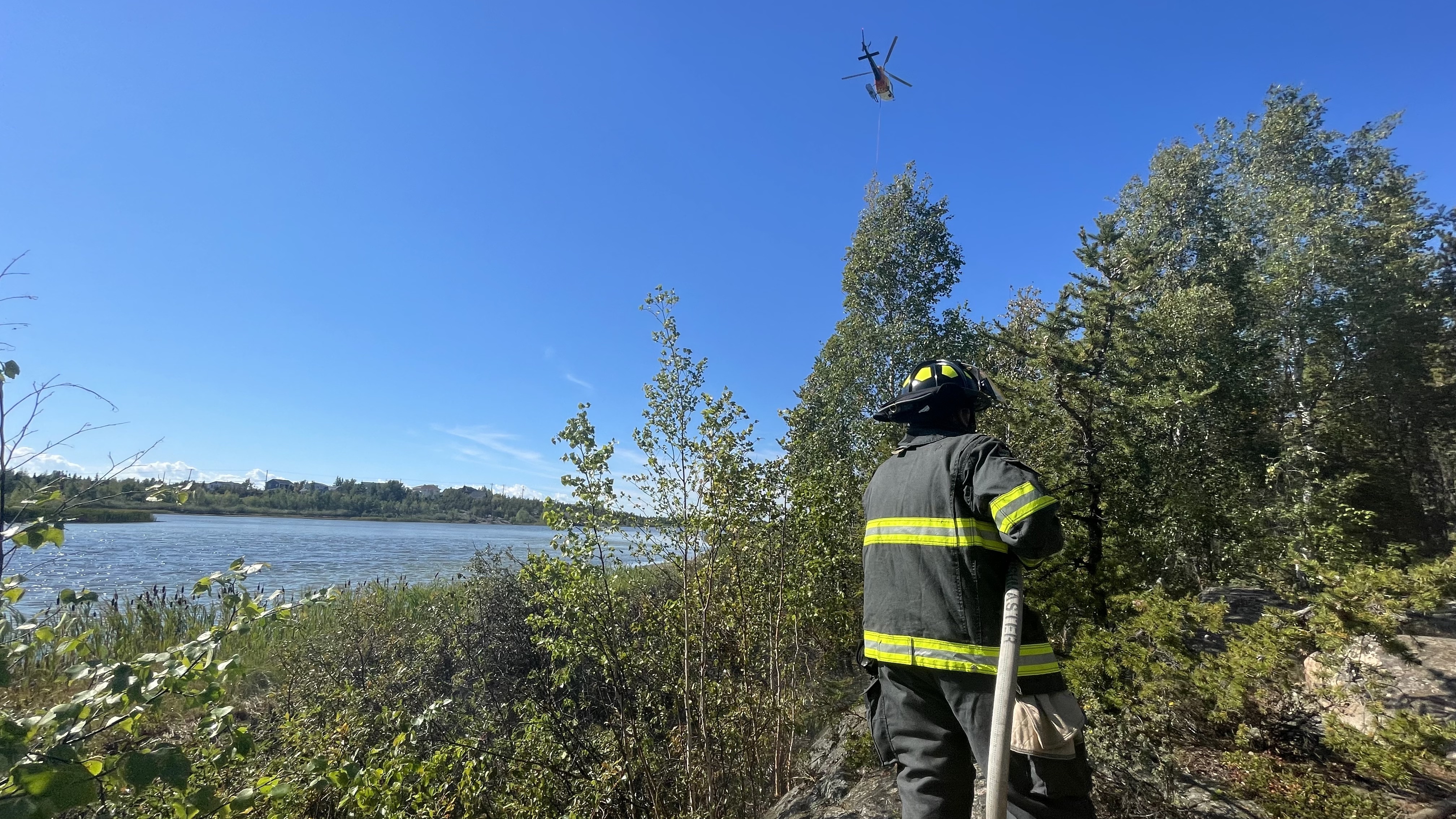 A Yellowknife firefighter and an ENR helicopter tackle a brush fire near Range Lake