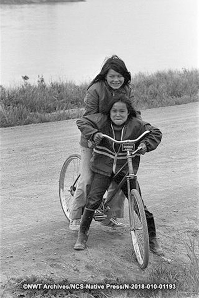 Leonie Lafferty and Barb Sambele on a bicycle in Fort Providence in June 1973