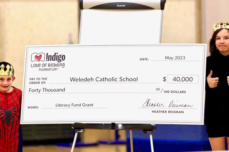 Weledeh Catholic School students Jack Nixon, left and Miyuki Voytilla, right pose with an Indigo Love of Reading Foundation promotional cheque. Talar Stockton/Cabin Radio