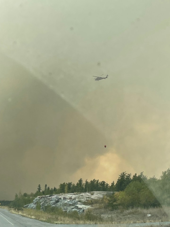 A helicopter heads to drops water on the fire as people evacuate Yellowknife on August 16, 2023. Photo: Nikki Rein