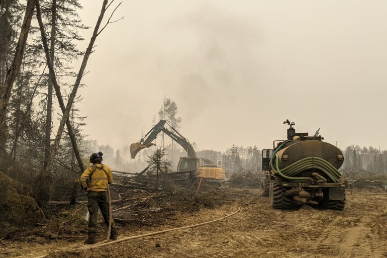 A firefighter works to extinguish hot spots along a containment line, with assistance from a water tender and excavator. Photo: Wood Buffalo National Park