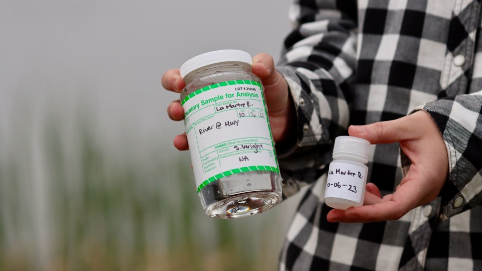 Wright holds water samples taken from the La Martre River. Chloe Williams/Cabin Radio