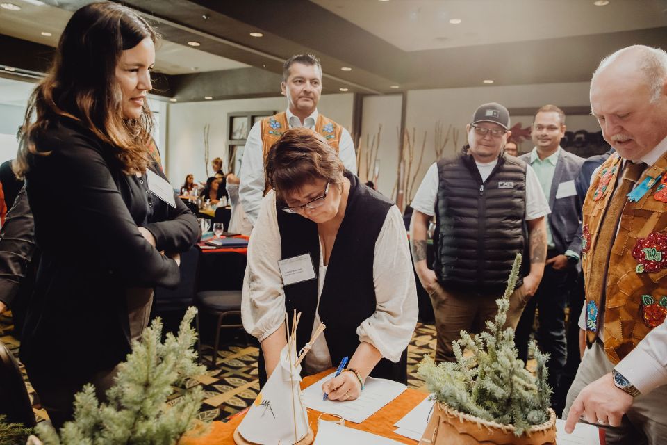 Melanie Norwegian, of Jean Marie River's Tthets'éhk'edélî First Nation, signs the PFP framework agreement in the presence of Tłı̨chǫ Grand Chief Jackson Lafferty (rear), NWT environment minister Shane Thompson (right) and others. Photo: Jamie Stevenson
