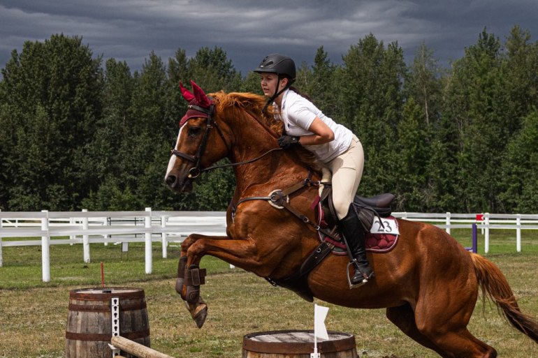 Riding student Jenny Murray jumps with horse Lexi at an Alberta horse show, with stormy skies in the background. Photo submitted by Caterina Walsh