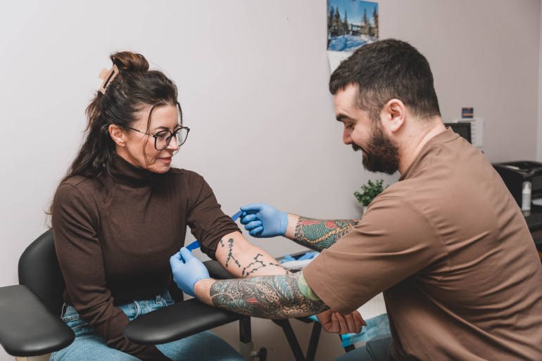 Caroline Newberry, left, manager of the communicable disease control unit within the Department of Health and Social Services, models waiting for a blood draw from registered nurse Christian Norwick. Sarah Pruys/Cabin Radio