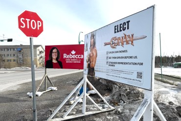 A sign for Conan the Barbarian appears net to a candidate's sign in Yellowknife during the 2025 federal election. Ollie Williams/Cabin Radio