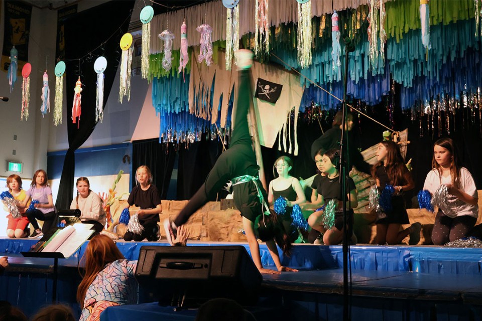 Students performing on stage. A young girl does a cartwheel.