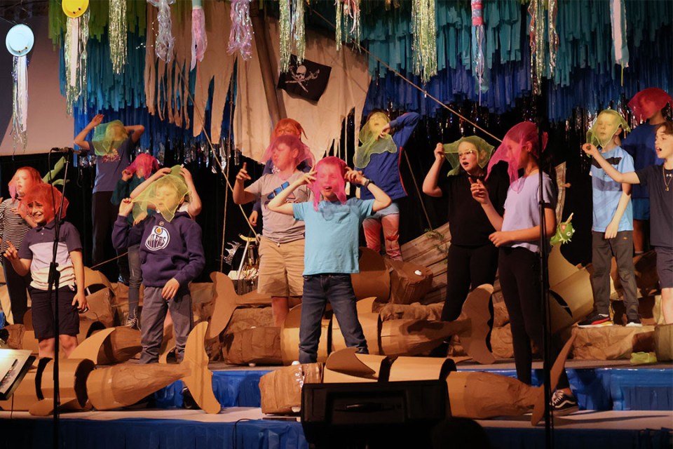 Children on stage covering their faces with a sheer handkerchief.