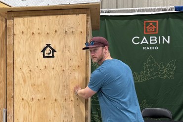Andrew Goodwin with the Cabin Radio outhouse. Ollie Williams/Cabin Radio