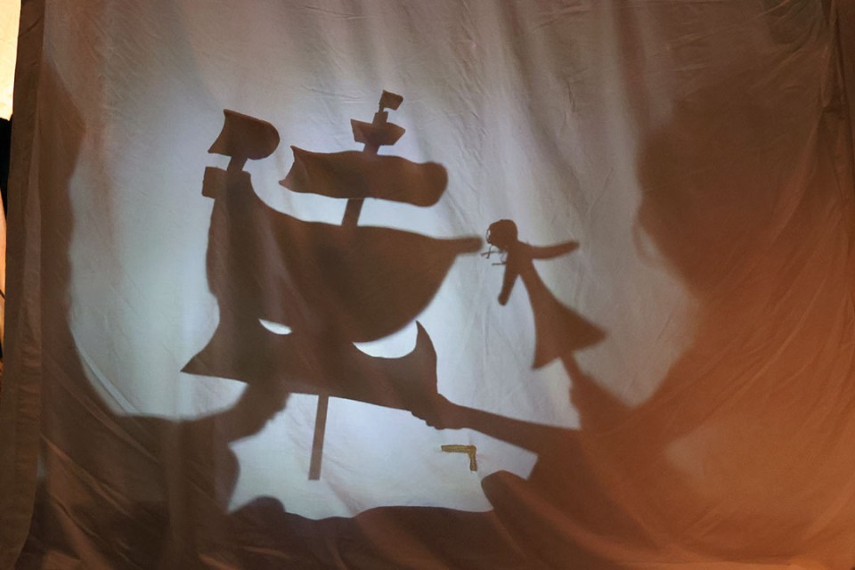 Shadow puppet show of ship and doll.