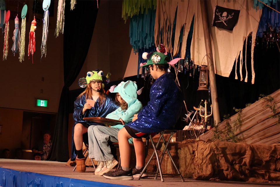 3 students on stage playing cards and dressed up as fish.