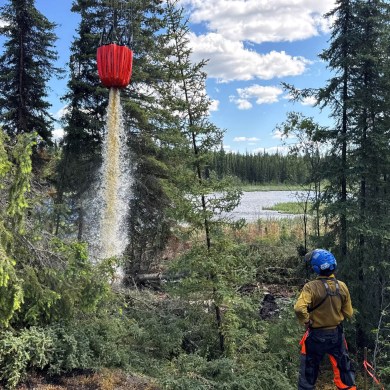 A firefighter watches as a bucket of water is dropped. Photo: NWT Fire