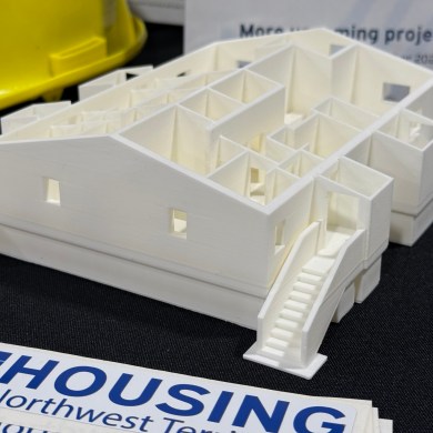 A model of a fourplex designed for the North is seen at a Housing NWT booth during the 2025 Arctic Development Expo in Inuvik. Ollie Williams/Cabin Radio
