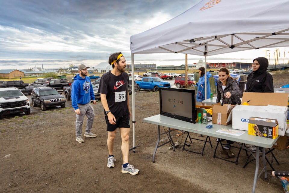 Kiyo Campbell, second from left, collects a medal from organizers after finishing the 10-km Midnight Sun Fun Run on June 21, 2025. Ollie Williams/Cabin Radio
