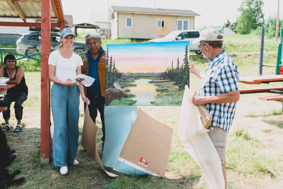 Fort Good Hope Chief Collin Pierrot gifts Julia Frith, far left, a painting by Bradley McNeely. Sarah Pruys/Cabin Radio
