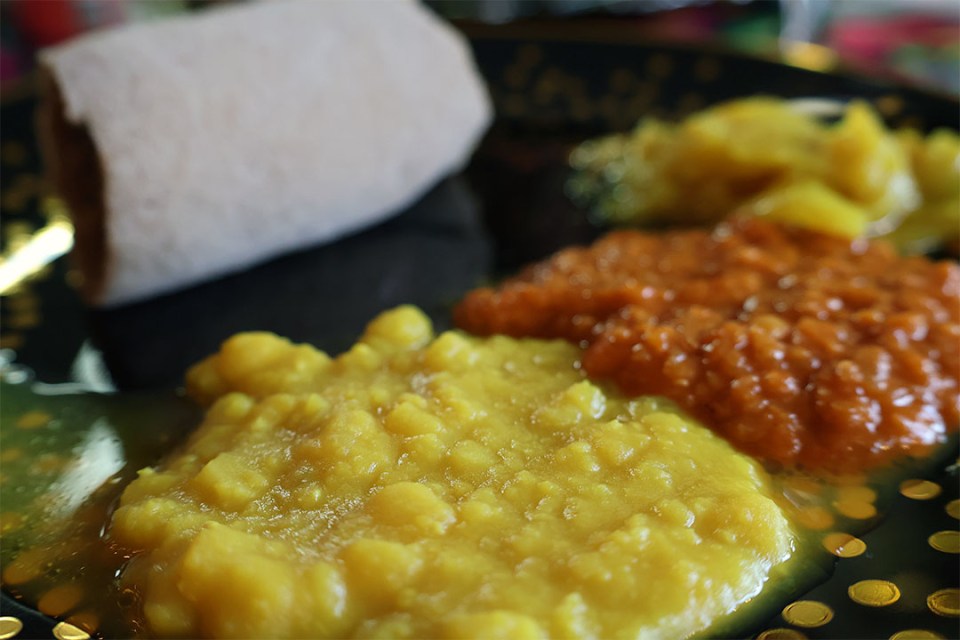 Close-up of trio of Ethiopian stews with rolled tef flatbread in background