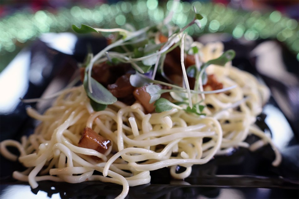Close-up of noodle dish topped with pork belly and greens