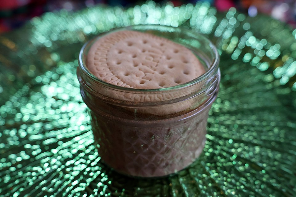Close-up of a small jar containing a dessert and topped with a biscuit.