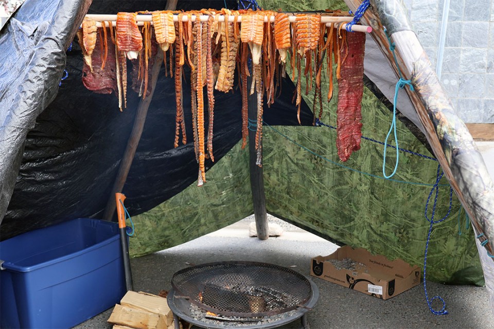 pieces of fish hang over a wood stove underneath a tent