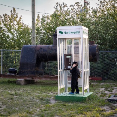 A child attempts a phone call from a Northwestel call box in the grounds of the Hay River Museum Society Heritage Centre. Ollie Williams/Cabin Radio