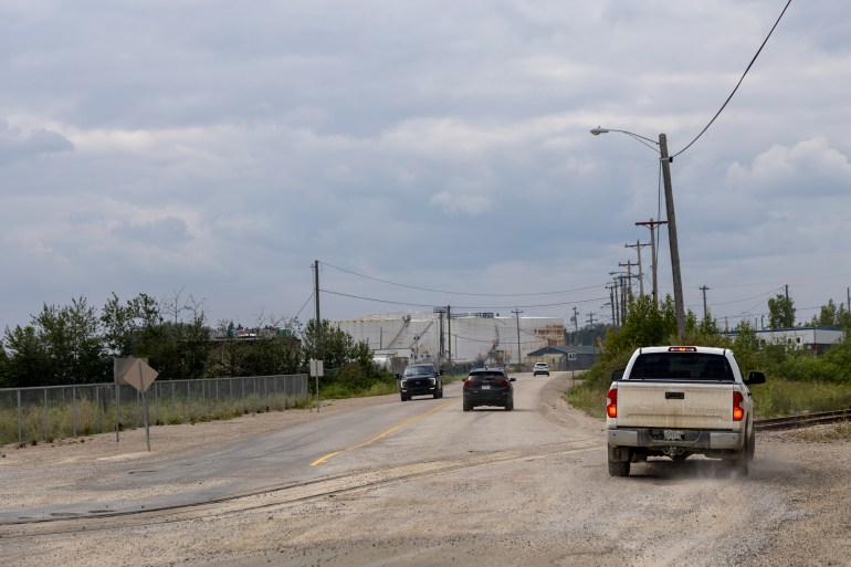 A white truck swerves to the side of the rail crossings, attempting to avoid the dip that the retired tracks have become.