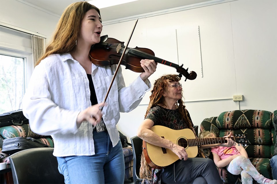 Two women play instruments (fiddle and guitar).