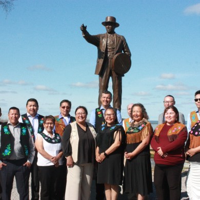 Members of the sixth Tłı̨chǫ Assembly in front of a statue of Chief Monfwi in Behchokǫ̀. Emily Blake/Cabin Radio