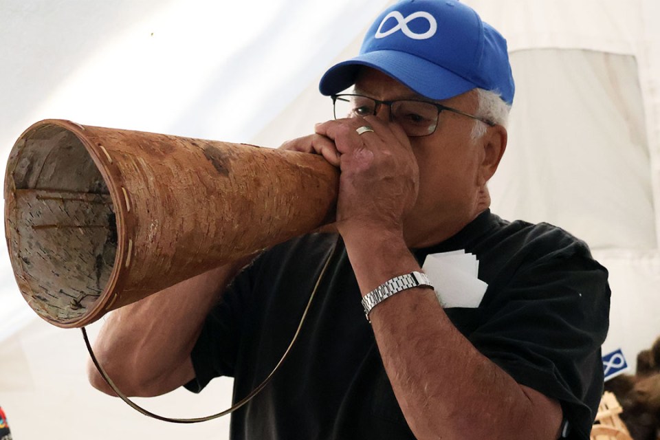 Man blows into a large birch-bark cone