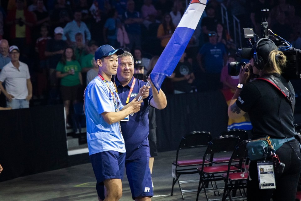 NWT minister responsible for sport, Vince McKay (right), hands the NWT's flag to Tony Shi at the 2025 Canada Games opening ceremony. Ollie Williams/Team NT