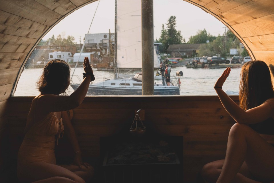 Girls wave as a sailboat passes by their sauna. Sarah Pruys/Cabin Radio