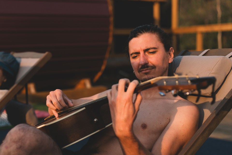 A guest plays guitar in a lounge chair before hitting the sauna. Sarah Pruys/Cabin Radio