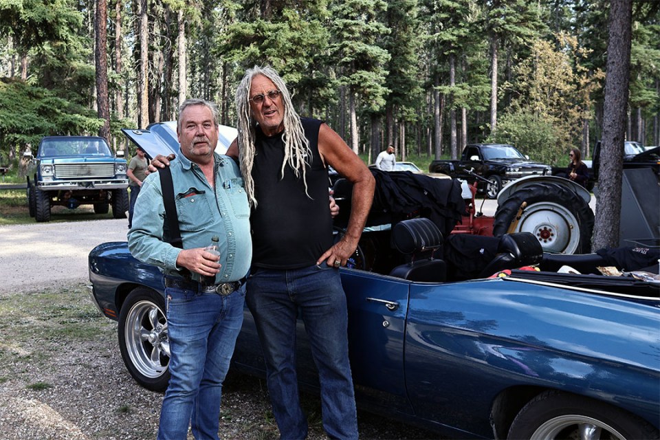 Two men pose in front of a vintage car
