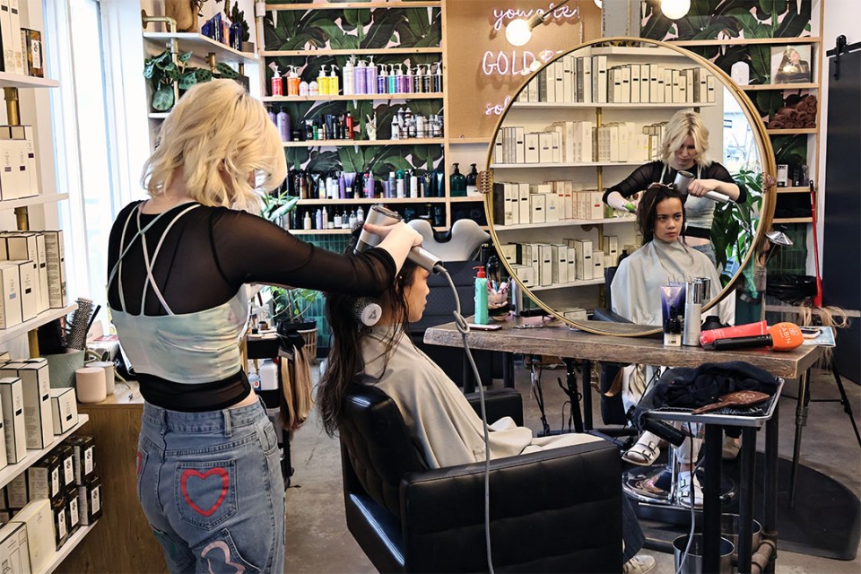 A hairstylist dries client's long hair inside a salon.