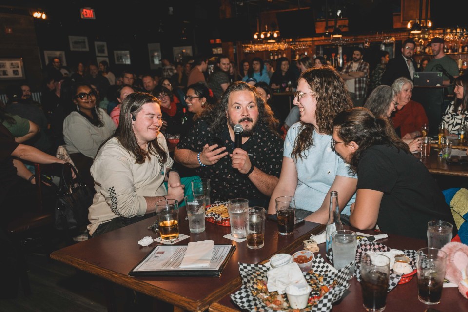 Cabin Radio’s Jesse Wheeler, second from the left, gives a lightning round word to a table and waits for the response. Sarah Pruys/Cabin Radio