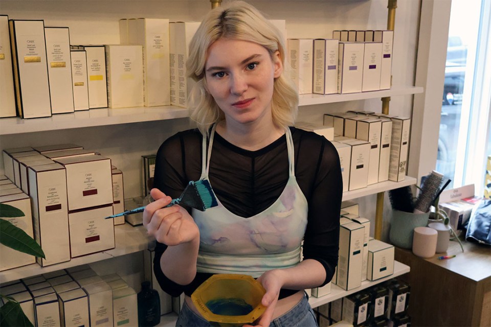 Blond woman holding a bowl and brush with teal hair dye.