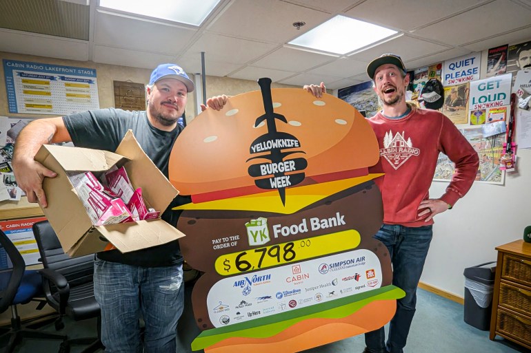 Mornings at the Cabin show hosts Jesse Wheeler, left, and Scott Letkeman pose with the 2025 Yellowknife Burger Week novelty cheque. In total, the fundraising event raised $6,798. Sarah Pruys/Cabin Radio