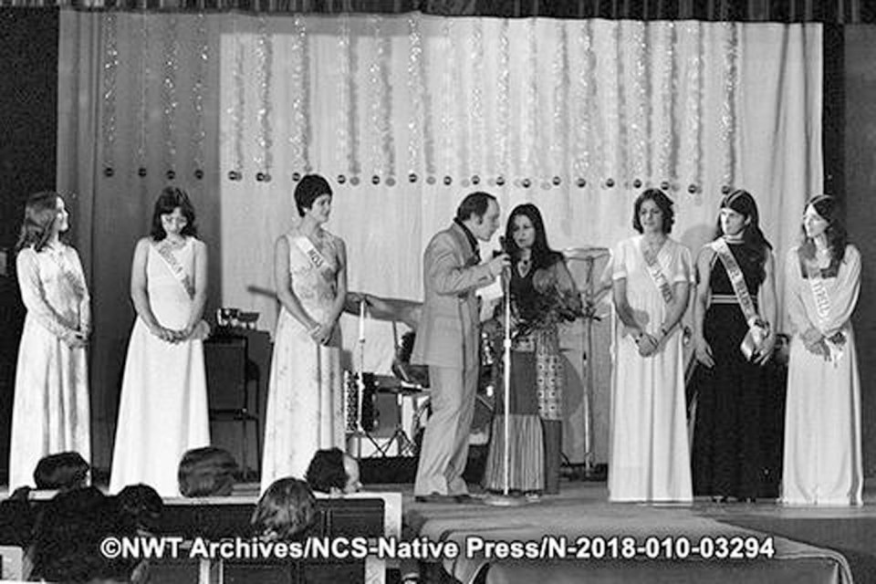 Participants in the 1976 Miss Teen NWT pageant. Names are given by the NWT Archives. From left: Sandra Kovatch (Hay River), Blandina Makkik (Frobisher Bay), Fawna Adrian (Yellowknife), master of ceremonies Wayne Collins, pageant co-chair Freda Hein, Pauline Oldfield (Yellowknife), Donna Hagen (Inuvik) and Dorian (Fort Smith). Published in Native Press newspaper on February 13, 1976. NWT Archives/Native Communications Society fonds - Native Press photograph collection/N-2018-010: 03294