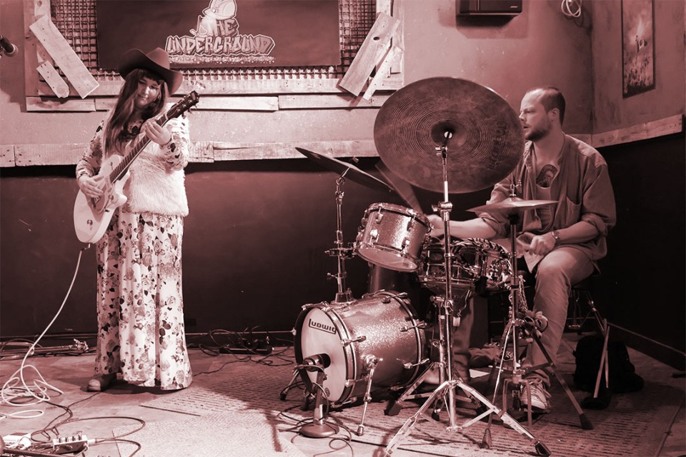 Woman with guitar and man on drums perform on stage