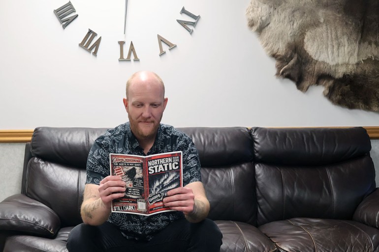 Man sits on a couch reading a magazine