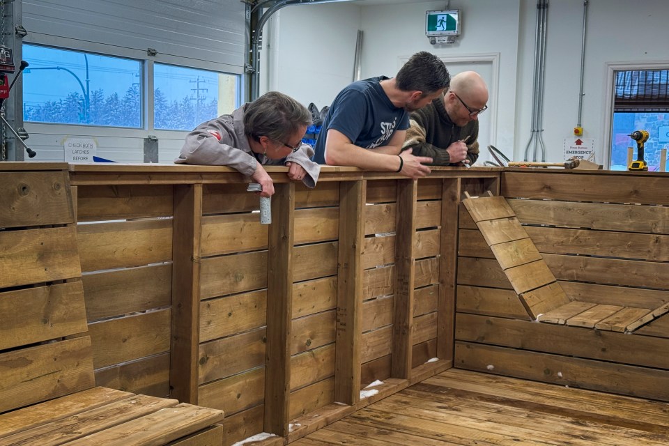Becca Denley, Adam Denley and Dwayne Wohlgemuth inspect connections between wooden modules. Ollie Williams/Cabin Radio