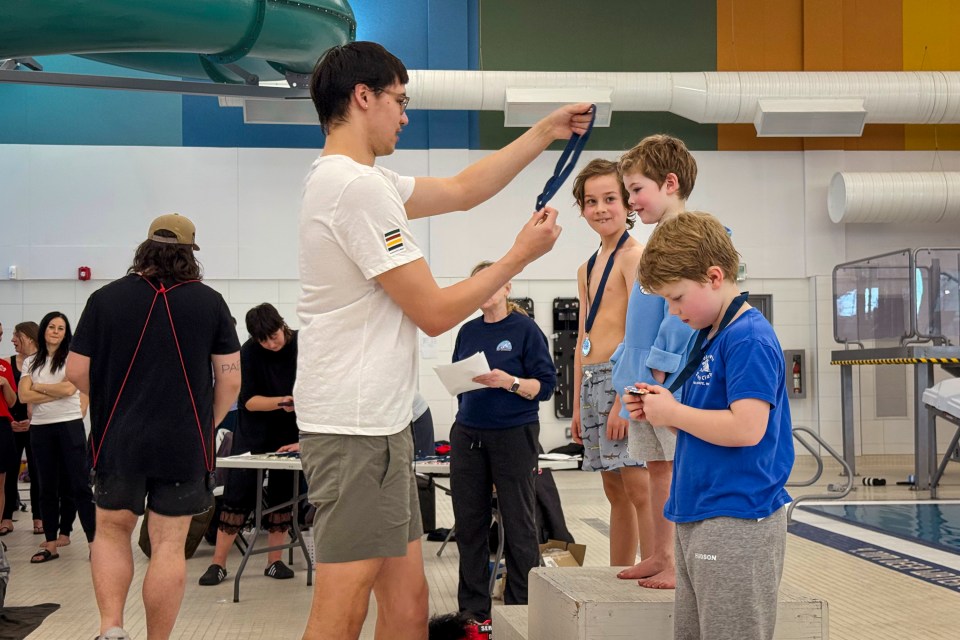 Markus Thormeyer presents young swimmers with medals at the NWT's territorial championships on February 22, 2026. Ollie Williams/Cabin Radio