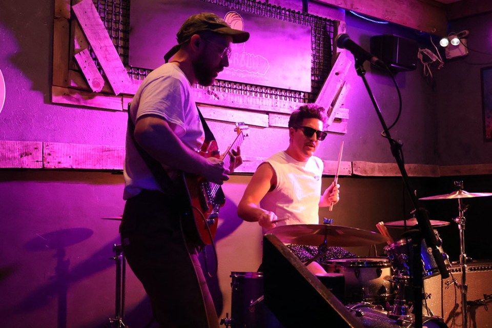 Man playing guitar and another man playing drums on stage