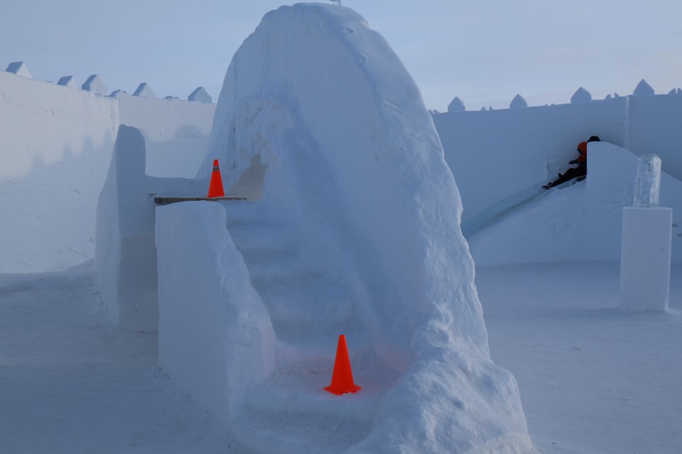 Stairs made of snow have orange hazard cones placed on them after melting.