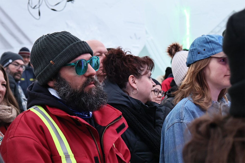 Close-up of a man in a red coat and sunglasses listening to a concert