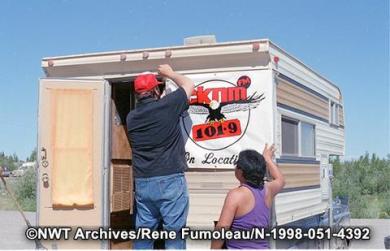 Peter Hope, right, and Percy Kinney hang a banner for CKLB (then known as CKNM) at the 1990 Dene National Assembly. NWT Archives/Rene Fumoleau fonds/N-1998-051: 4392