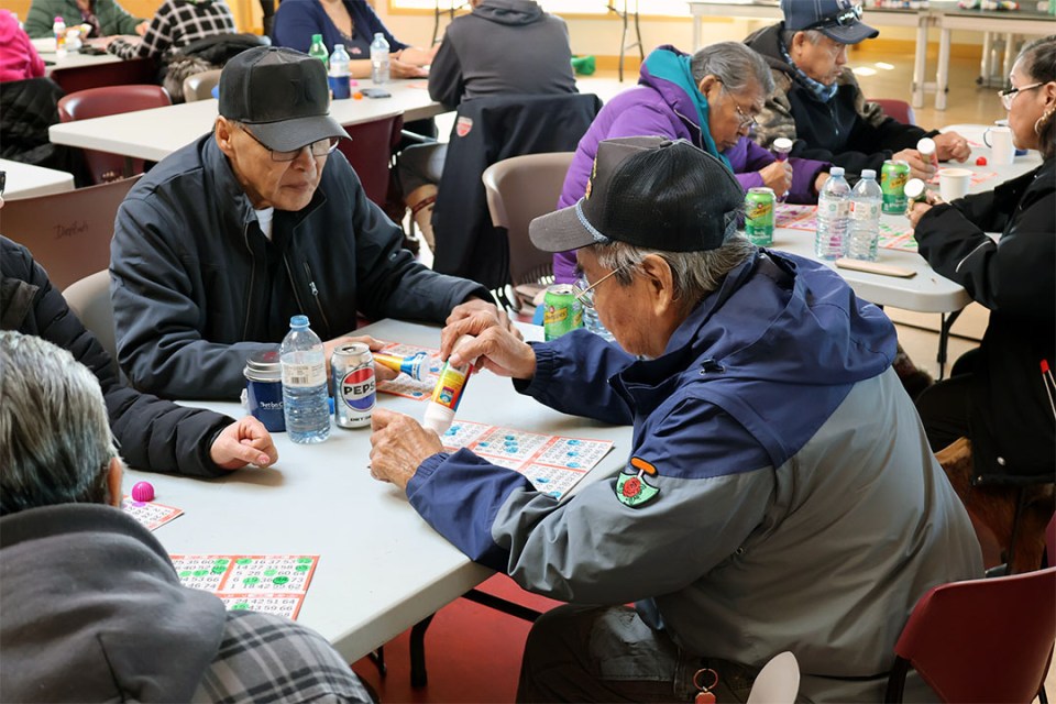 Two men seated at a table dabbing bingo cards.