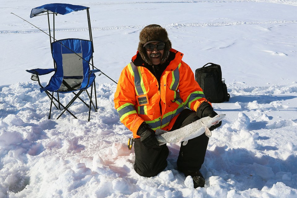Man standing on a snow-covered frozen lake holds a fish he caught