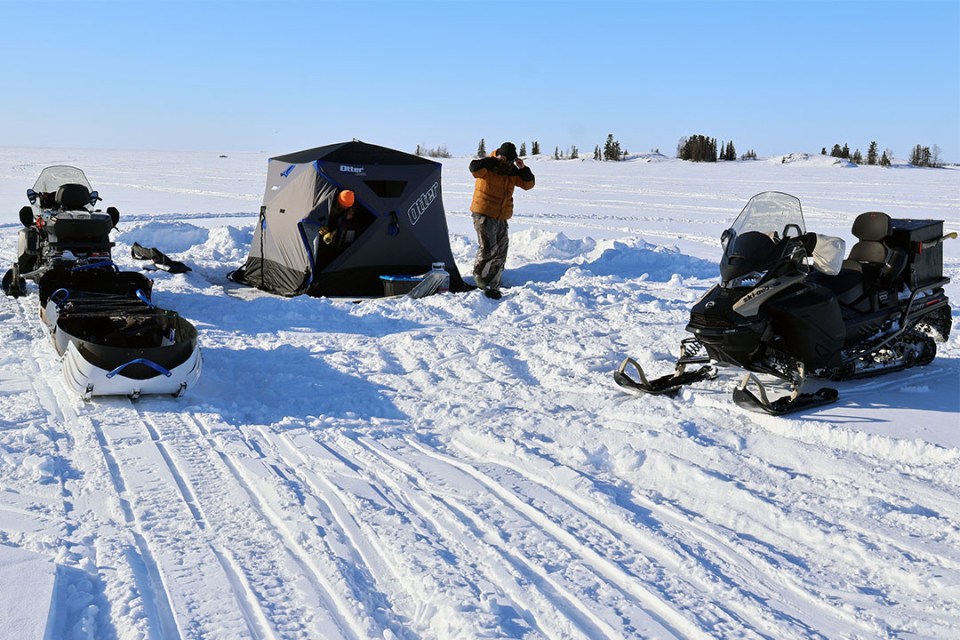 tent and skidoos on the lake. 2 men can be seen exiting
